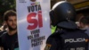 Сторонник независимости Каталонии с плакатом "Проголосуй за "Да" перед испанским полицейским. Барселона, 20 сентября 2017 года